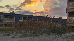 A beach with sand, a wooden fence, and two buildings with balconies.