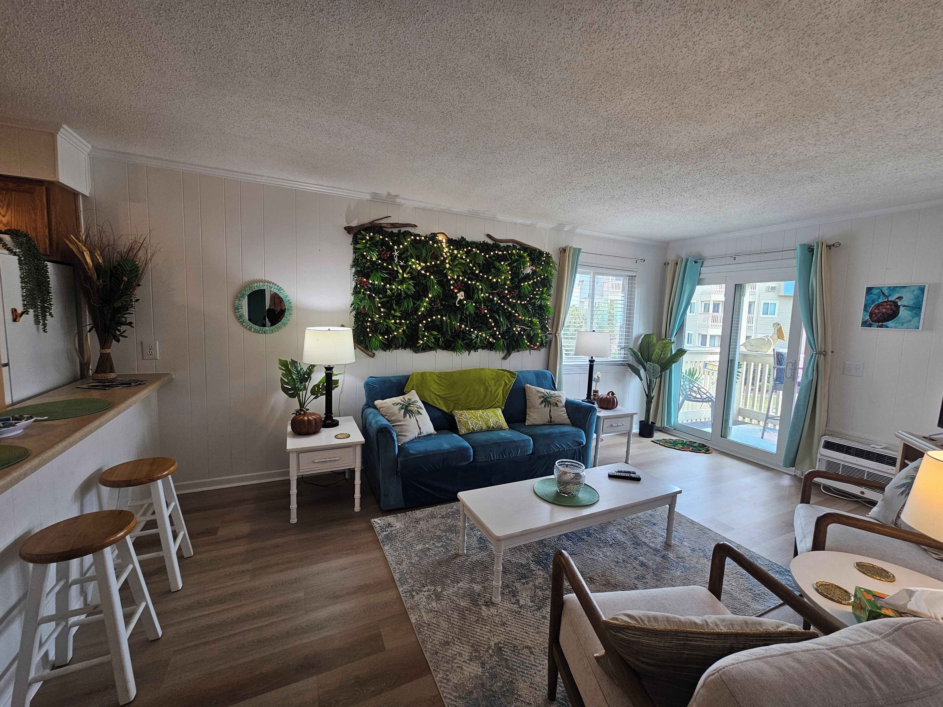 A cozy living room with a blue sofa, a coffee table, and a dining area with stools.
