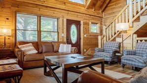 Un acogedor interior de cabaña con paredes de madera, un sofá, una mesa de centro y sillones a cuadros.