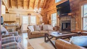 A log cabin interior with a fireplace, wooden walls, a sofa, and a dining table. - Bear Creek Way by Avantstay Hot Tub, Game Room, Air Hockey, Near Dollywood & Smoky Trails (Sevierville)