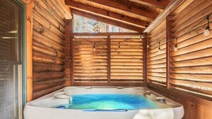 Interior de una cabaña de troncos con jacuzzi, paredes de madera y una ventana.