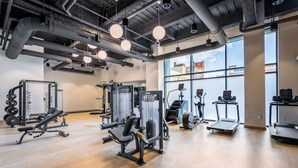 A gym with various exercise equipment, large windows, and a high ceiling with exposed ductwork. - King Bed Comfort | Free Parking | UPMC, Pitt & CMU (Pittsburgh)