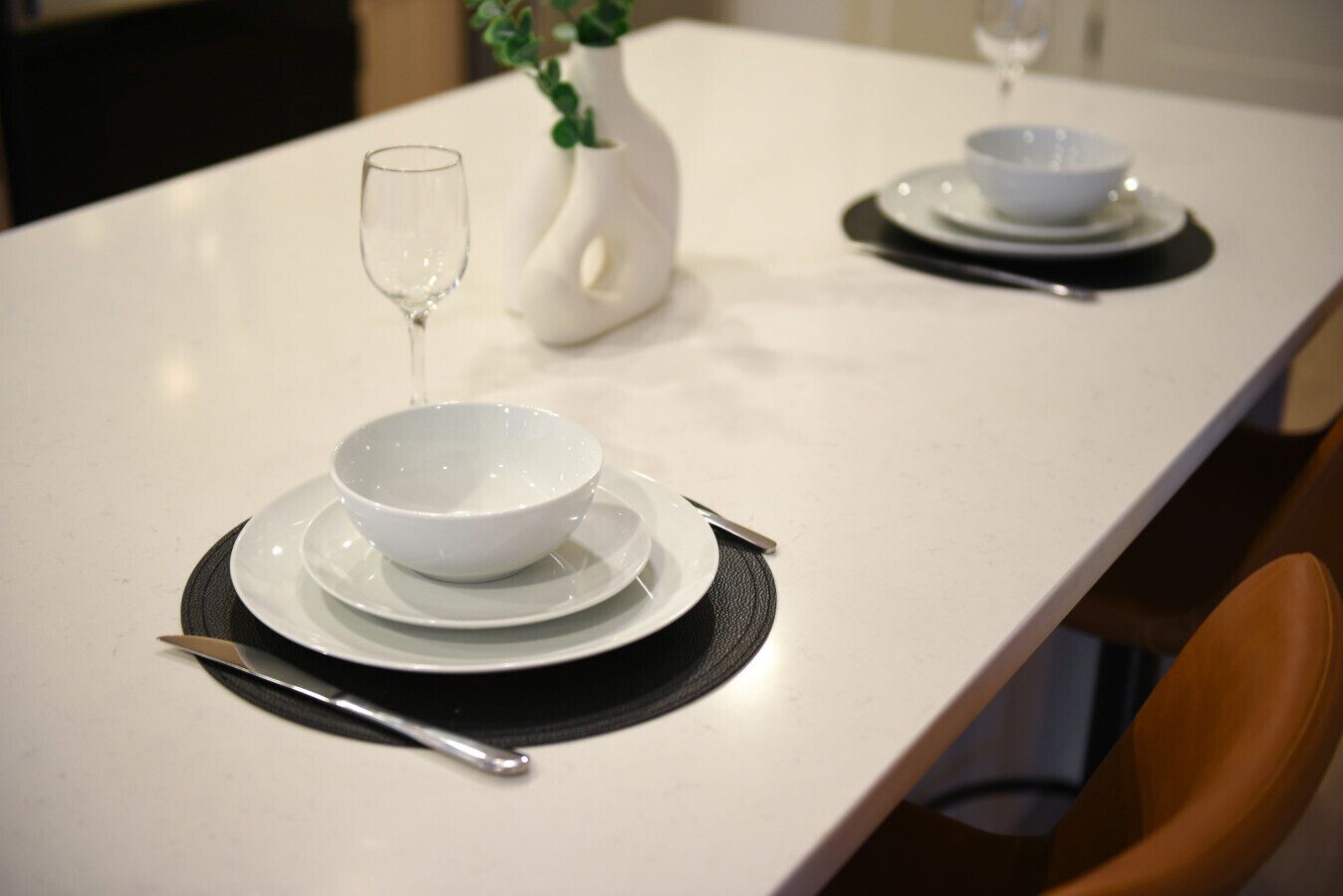Een eettafel gedekt met witte borden, kommen en bestek.