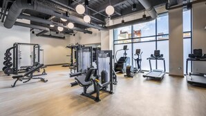 Une salle de sport moderne dotée de divers appareils d’exercice, de grandes fenêtres et d’un plafond haut avec des conduits apparents.