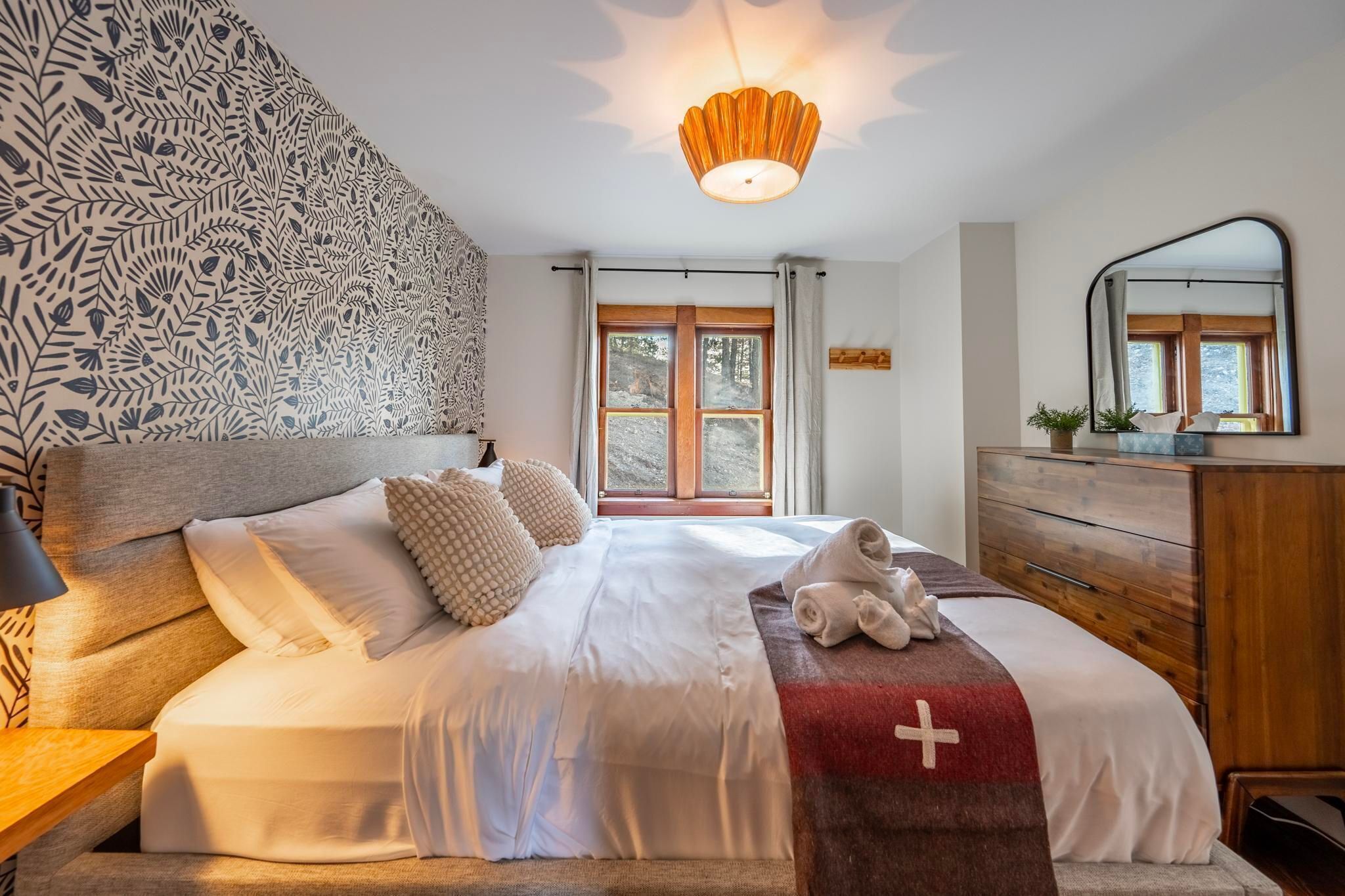 A bedroom with a bed, a wooden dresser, a mirror, and a window with curtains.
