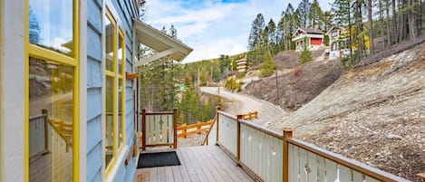 Eine Holzdielen-Terrasse mit Blick auf einen bewaldeten Hügel und ein weit entferntes Haus.