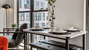 A modern dining area with a large window, a dining table set with plates and a vase of flowers, and a bench.