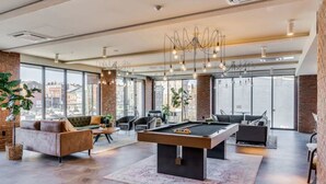 A spacious living area with a pool table, comfortable seating, large windows, and a modern chandelier.