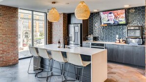 A modern kitchen with a large island, bar stools, a TV, and a city view.