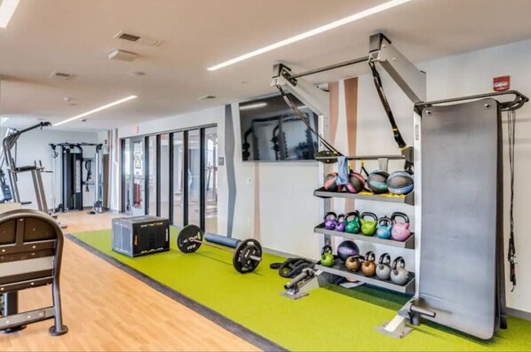 Un gimnasio con equipo de levantamiento de pesas, kettelbells y máquinas de ejercicio.