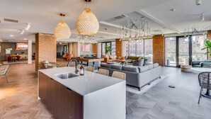 Una cocina moderna con una isla central, un comedor con una mesa larga y una sala de estar con sofás y una mesa de centro.