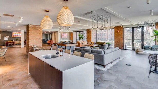 A modern kitchen with a central island, a dining area with a long table, and a living area with sofas and a coffee table.