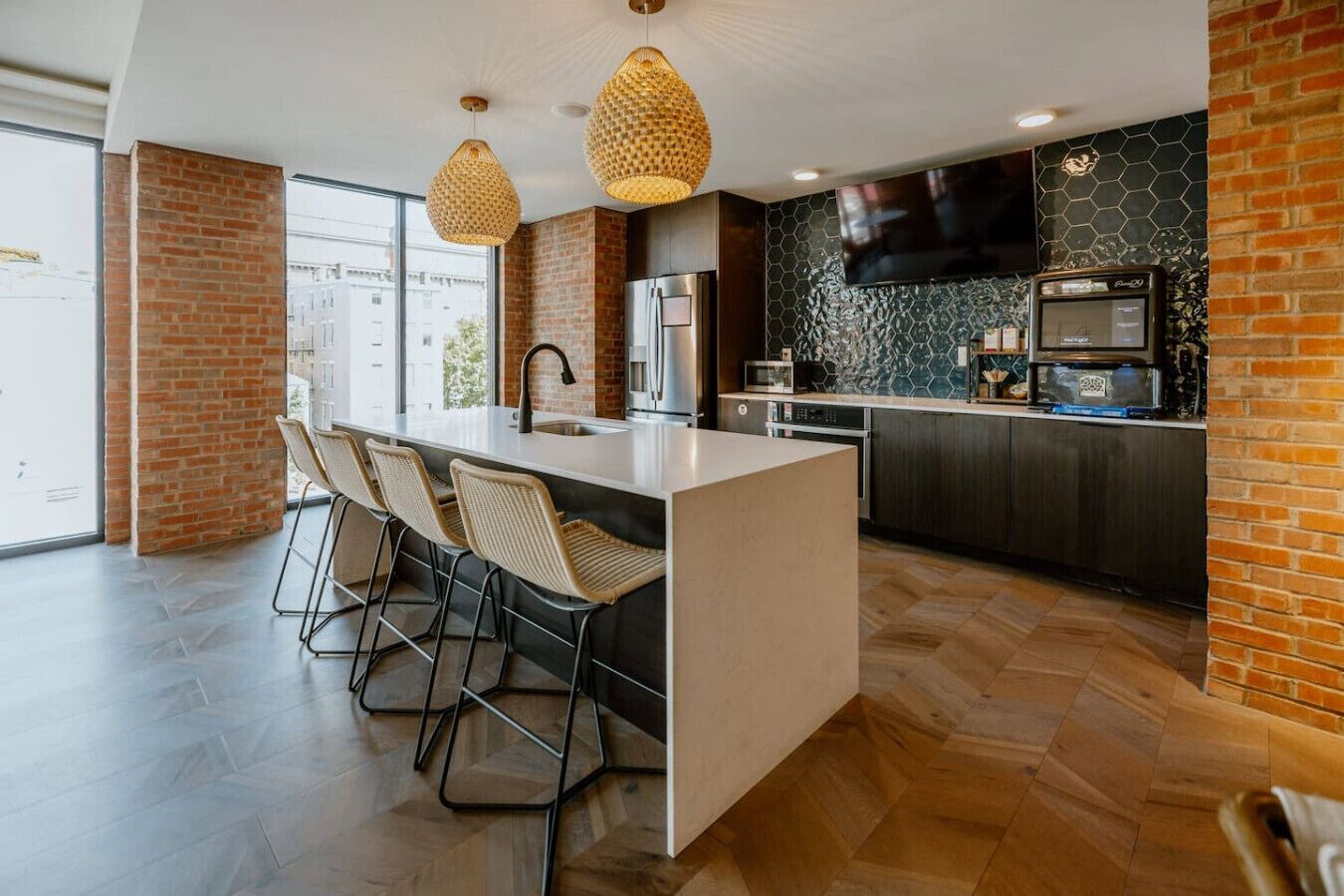 Uma cozinha moderna com uma ilha central, banquetas, uma televisão de tela plana e uma parede de destaque em tijolo.