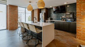 Uma cozinha moderna com uma ilha central, banquetas, uma televisão de tela plana e uma parede de destaque em tijolo.