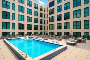A hotel with a swimming pool, lounge chairs, and a tiled floor.