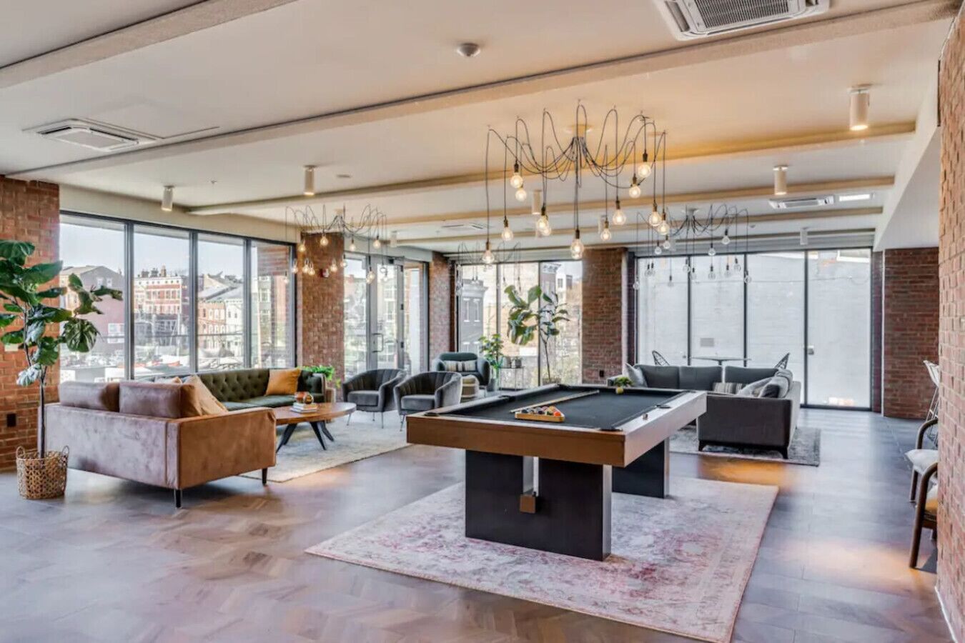 Uma sala de estar espaçosa com mesa de bilhar, assentos confortáveis, amplas janelas e um lustre moderno.