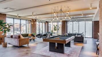 Uma sala de estar espaçosa com mesa de bilhar, assentos confortáveis, amplas janelas e um lustre moderno.