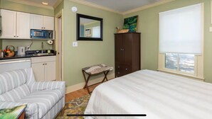 Un dormitorio con cama, una zona de estar pequeña, un armario y una kitchenette.