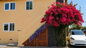 A yellow building with a white car parked in front, a number '8956' on the wall, and a large pink flowering plant. - Central San Gabriel - Sleeps 4, Pet Friendly Unit (San Gabriel)