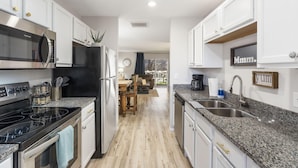 Una cocina moderna con armarios blancos, un refrigerador negro, electrodomésticos de acero inoxidable y encimeras de granito, además de un comedor con vistas.