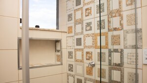 A bathroom with a tiled wall featuring a variety of square patterns and a shelf unit. - Comfort Suite 203 (Centro Diamantina)
