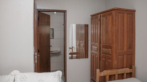 A bedroom with a wooden wardrobe, a bed with a floral duvet, and a mirror reflecting the room. - Comfort Suite 203 (Centro Diamantina)