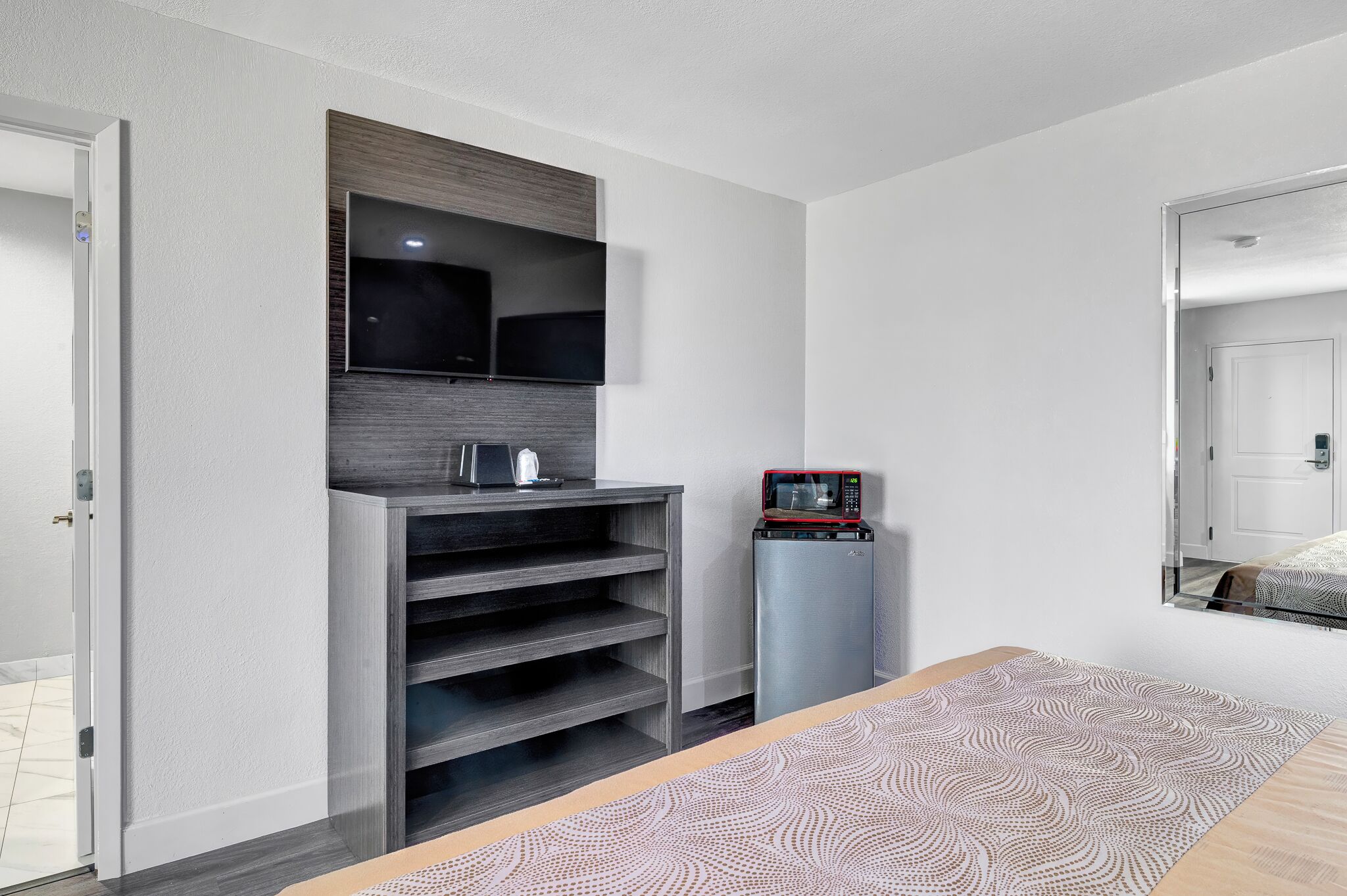 A modern hotel room with a built-in TV, a minibar, and a patterned rug.
