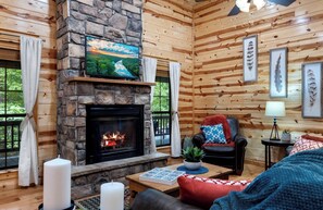 A cozy cabin interior with a stone fireplace, wooden walls, a comfortable seating area, and framed artwork. - 1 Br - 1 Ba - Sleeper Sofa - Sleeps 4 - Hot Tub (Broken Bow)