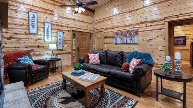 A log cabin interior with a leather couch, a wooden coffee table, and a ceiling fan.