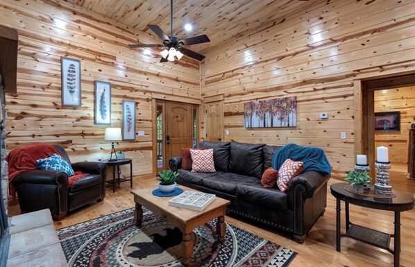 A log cabin interior with a leather couch, a wooden coffee table, and a ceiling fan.