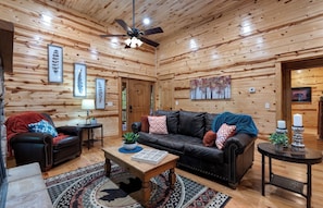 Ein Holzblockhaus-Interieur mit einer Ledersofa, einem Holztisch und einem Deckenventilator.