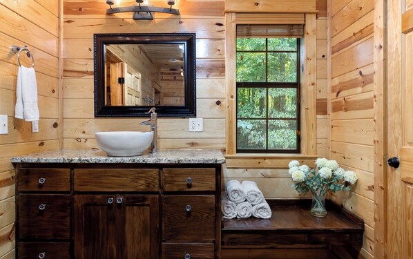 Baño de cabaña de madera con lavamanos, espejo y ventana.