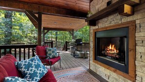 A covered outdoor area with a stone fireplace, a barbecue grill, and a seating area with cushions.