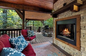 A covered outdoor area with a stone fireplace, a barbecue grill, and a seating area with cushions.