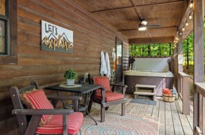 A wooden cabin with a hot tub, a table with chairs, and a sign that reads 'LET'S ENJOY'.