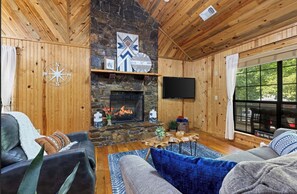 Ein gemütliches Wohnzimmer mit Kamin aus Stein, Holzwänden und einem großen Fenster.