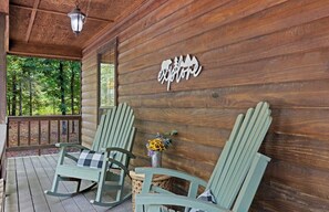 Eine Holzhütte mit Veranda, zwei Schaukelstühlen, einem kleinen Tisch mit Blumenvase und einem Schild mit der Aufschrift 'explore'.