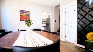 A dining area with a wooden table, chairs, a vase with flowers, and a painting on the wall.
