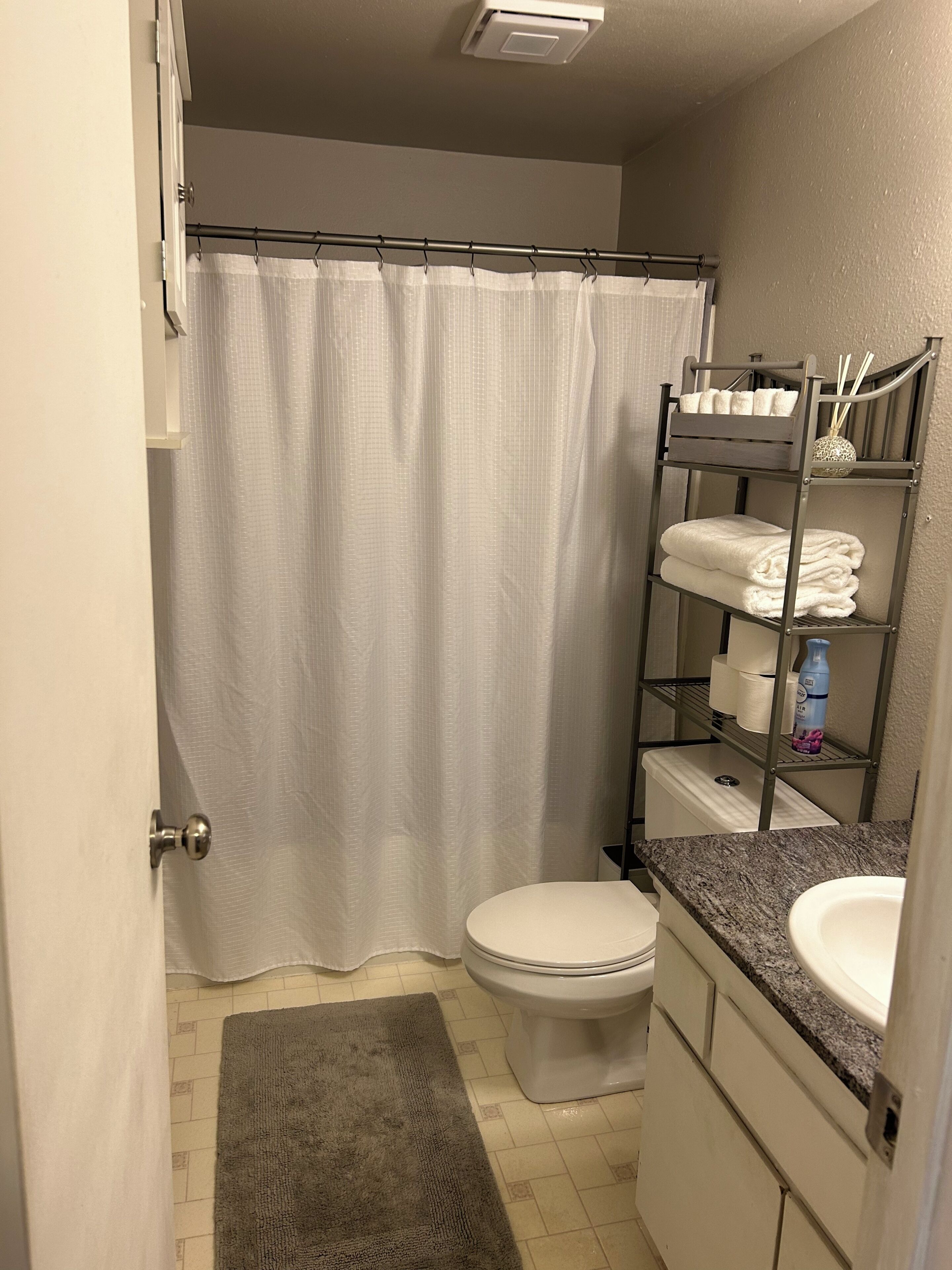 A bathroom with a shower curtain, toilet, sink, and towel rack.