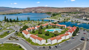 A hotel with a central swimming pool, surrounded by a courtyard with trees and a parking lot.