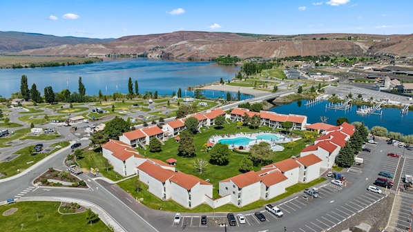 A hotel with a central swimming pool, surrounded by a courtyard with trees and a parking lot.