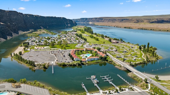 An aerial view of a lakeside resort with a swimming pool, parking areas, and a bridge connecting to the mainland.