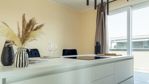 Una cocina moderna con encimera blanca, un jarrón con plumas de miscanthus, dos copas de vino y una silla negra.
