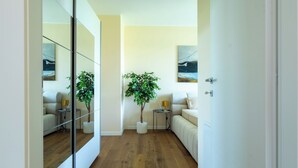 Una sala de estar moderna con suelo de madera, un espejo grande, una planta en maceta, un sofá y una mesita de noche con una lámpara.