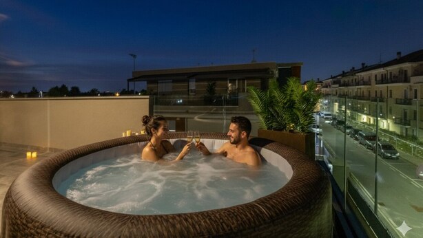 Una pareja en un jacuzzi en una terraza en la azotea con vistas a la ciudad al atardecer.