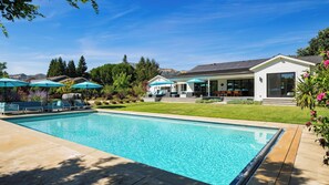 A swimming pool with lounge chairs and umbrellas, a patio area with outdoor furniture, and a house with a covered patio. - Luxe, Pool, Spa, Fire Pit, Game Room, Piano Sonoma Pool Retreat by Avantstay (Kenwood)