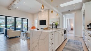 A modern kitchen with a marble island, pendant lights, and a large window overlooking a patio. - Luxe, Pool, Spa, Fire Pit, Game Room, Piano Sonoma Pool Retreat by Avantstay (Kenwood)