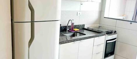 A modern kitchen with white cabinets, a stainless steel refrigerator, a microwave, a sink with a faucet, and a stove.