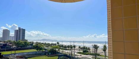 Un balcon avec vue sur une plage, des palmiers et des bâtiments situés au loin.