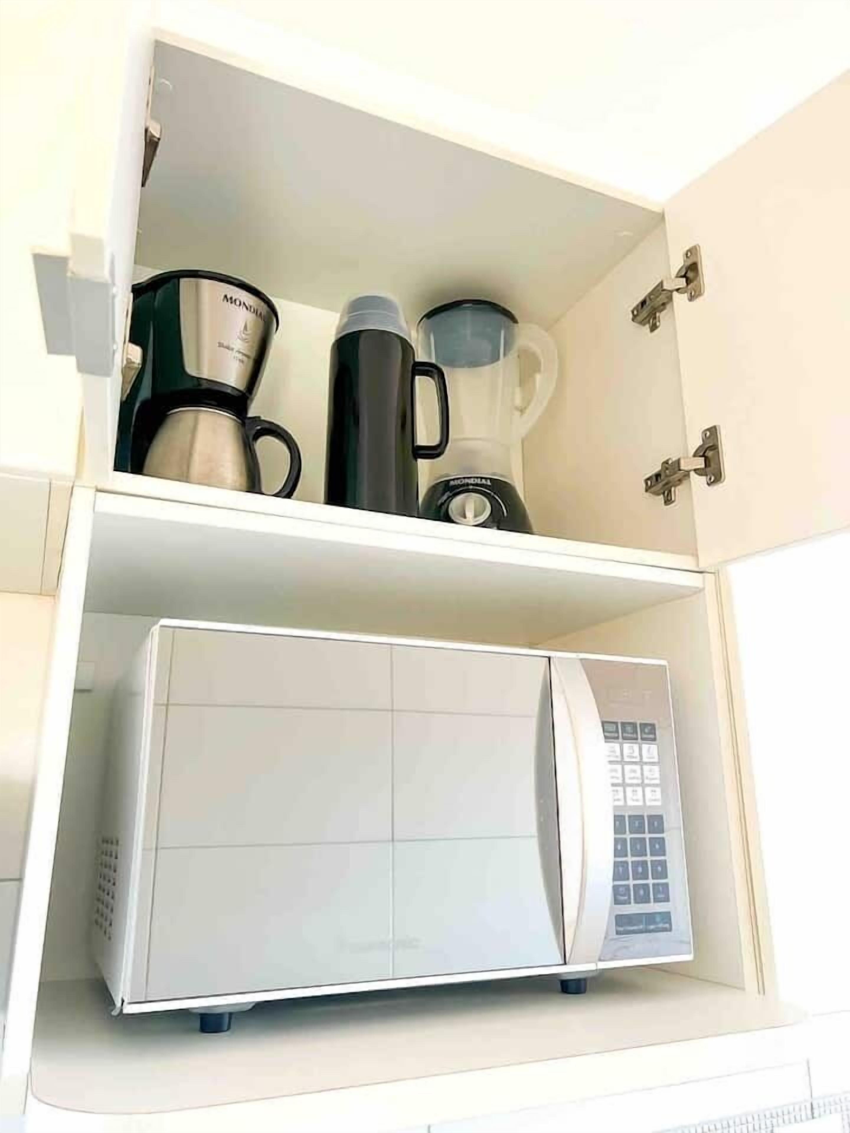 A kitchen with a white microwave on the lower shelf and a coffee maker and blender on the upper shelf.